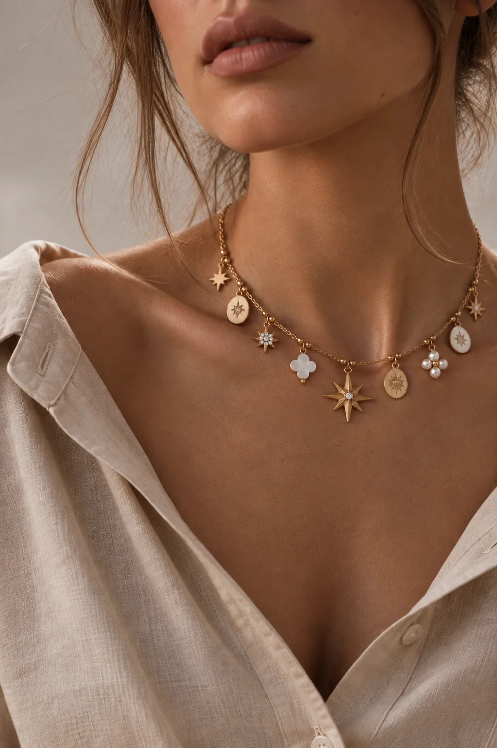 Elegante Charm-Halskette in Gold mit Sternen-, Kleeblatt- und Perlmutt-Anhängern am Dekolleté.