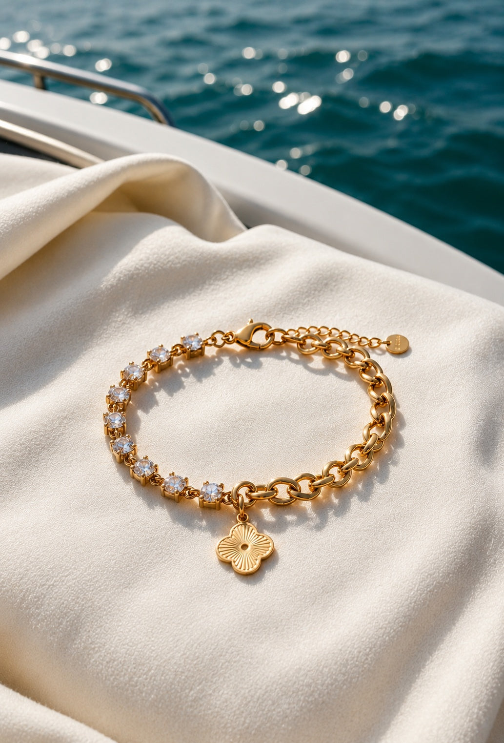 Elegantes goldfarbenes Damenarmband mit Zirkonia, Gliederkette und Kleeblatt-Anhänger auf einer Yacht – hochwertiger Schmuck im maritimen Lifestyle.