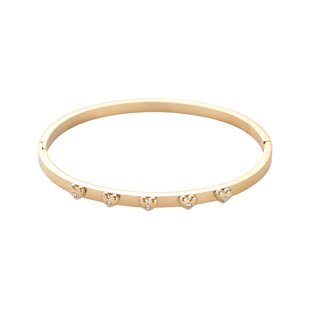 Goldener flacher Armreif Modell Pure aus 14k vergoldetem Edelstahl mit kleinen Herzen und funkelnden Kristallen auf weißem Hintergrund