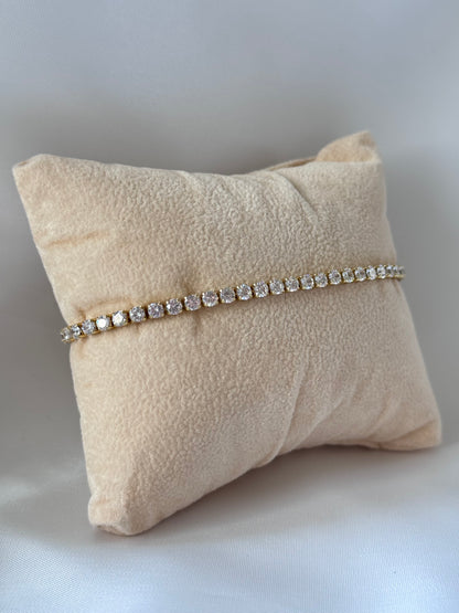 Tennisarmband aus kupfervergoldetem Metall mit funkelnden Zirkonia-Steinen, verstellbarem Schiebeverschluss und elegantem, glänzendem Design.