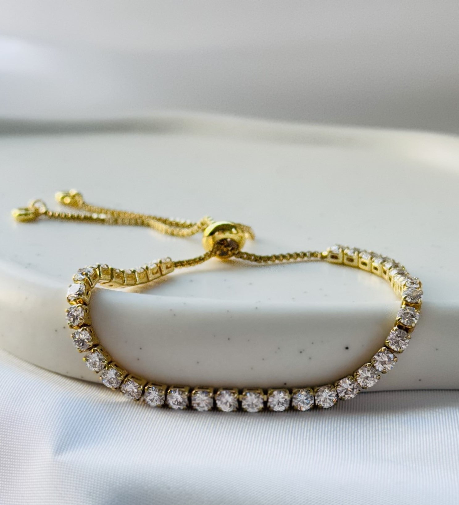 Tennisarmband aus kupfervergoldetem Metall mit funkelnden Zirkonia-Steinen, verstellbarem Schiebeverschluss und elegantem, glänzendem Design.