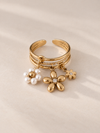 Detailansicht des Adele Rings mit Anhängern aus Goldblüten und einer feinen Perlenblüte auf hellem Untergrund.