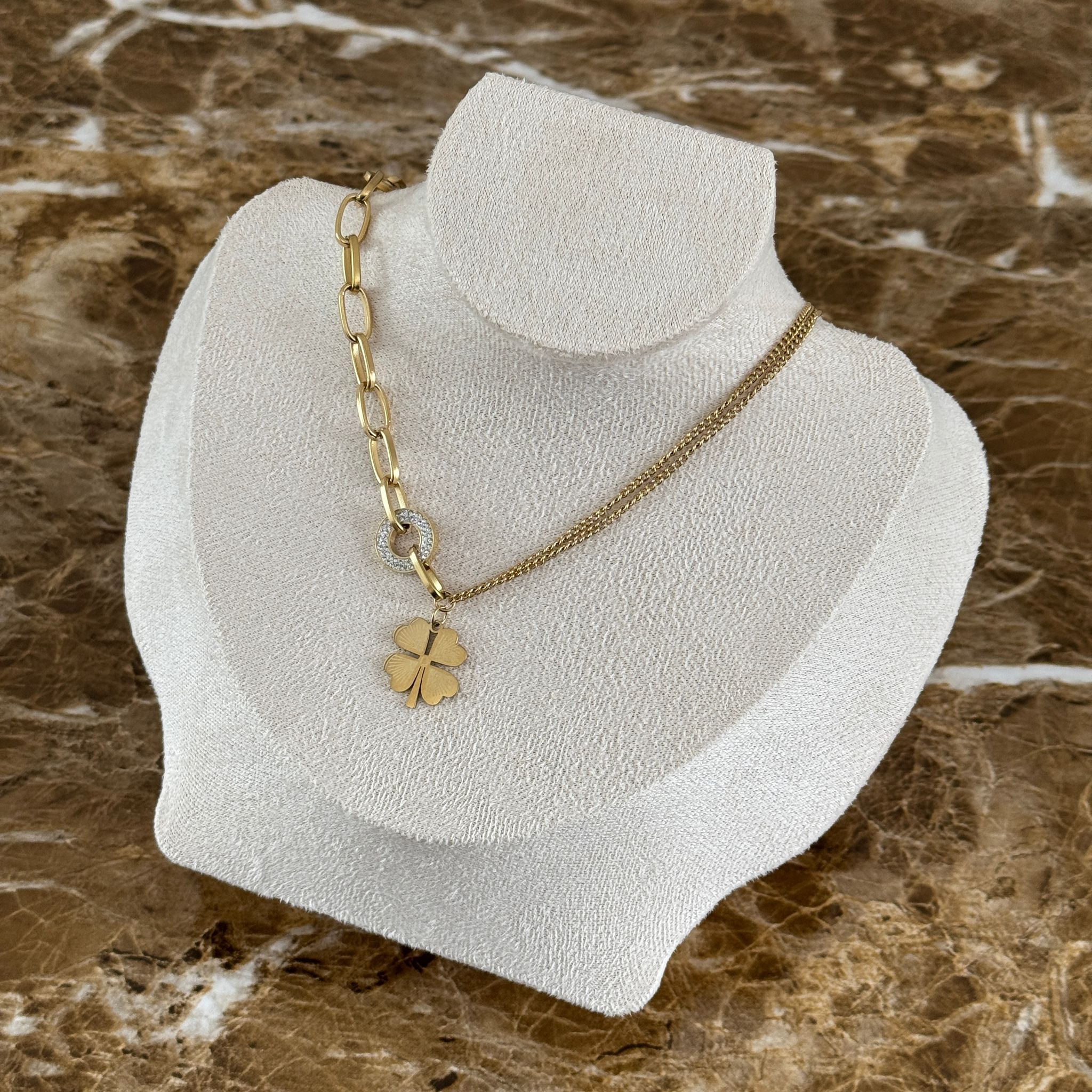 Nahaufnahme des Amara Anhängers: Ein funkelnder, mit Zirkonia-Steinen besetzter Ring hält ein goldenes Kleeblatt an der 14k vergoldeten Edelstahlkette.