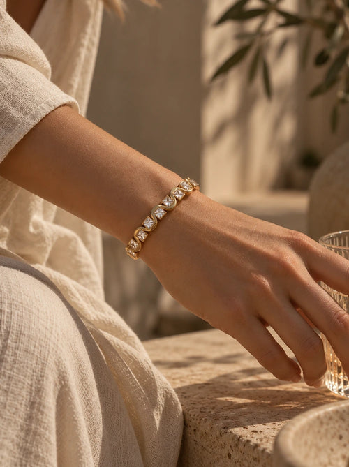 Frau trägt den Ariella Armreif in Gold mit Zirkonia am Handgelenk zu einem cremefarbenen Outfit
