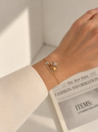 Celestial Armband mit Sicherheitsnadel-Motiv und Sternen getragen am Handgelenk über einer Zeitung.