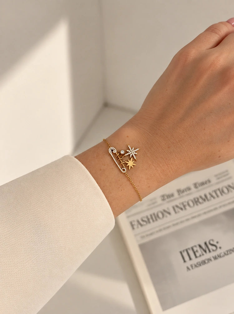 Celestial Armband mit Sicherheitsnadel-Motiv und Sternen getragen am Handgelenk über einer Zeitung.