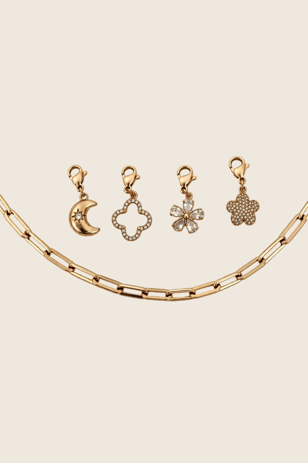 Vier vergoldete Charm-Anhänger mit Karabiner (Mond, Kleeblatt, Zirkonia-Blüte, Glitzerblume) arrangiert über einer groben Gliederkette.