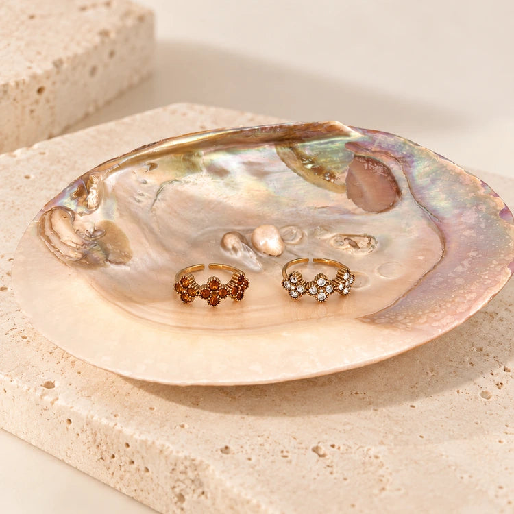 Die verstellbaren Crystal Bloom Ringe in den Farbvarianten Gold und Braun präsentiert in einer Perlmutt-Muschel.