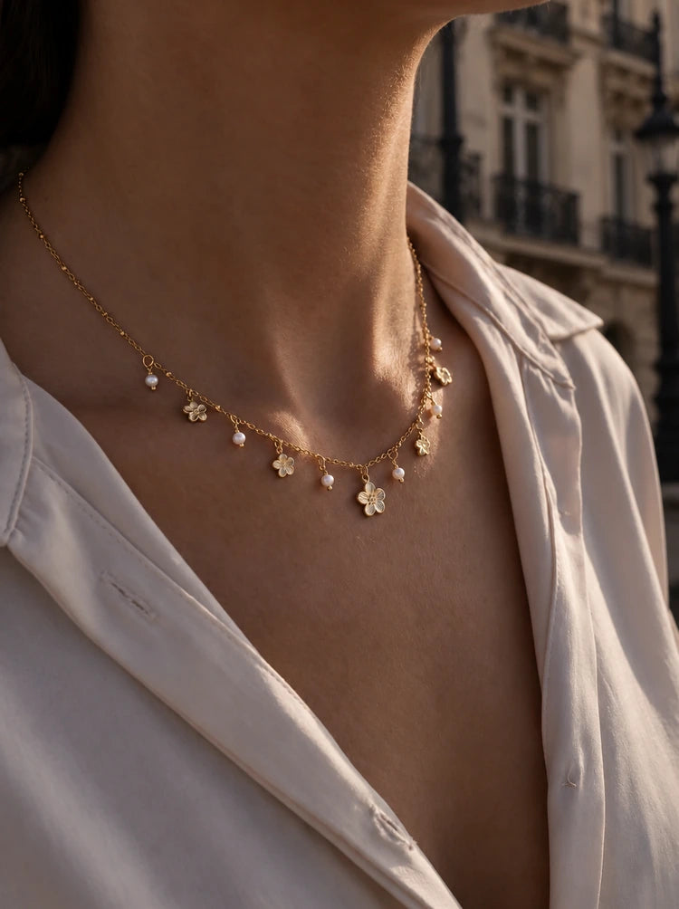Frau trägt die Fiora Halskette in Gold mit Blüten-Charms und Perlen zur cremefarbenen Bluse