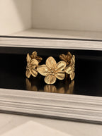 Nahaufnahme des verstellbaren Florencia Bangle Armreifs mit feingestanzten Blütenblättern dekoriert auf einem Buch.