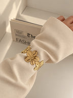 Florencia Bangle Armreif aus 14k vergoldetem Edelstahl mit Blumenmotiv getragen über dem Ärmel eines beigefarbenen Blazers.
