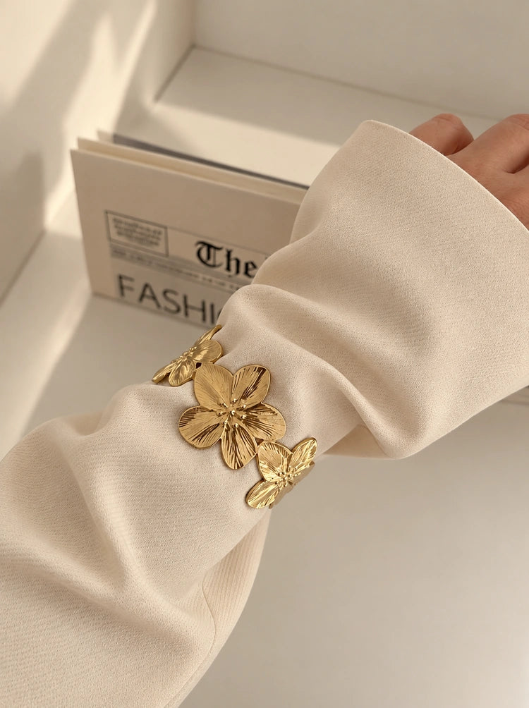 Florencia Bangle Armreif aus 14k vergoldetem Edelstahl mit Blumenmotiv getragen über dem Ärmel eines beigefarbenen Blazers.