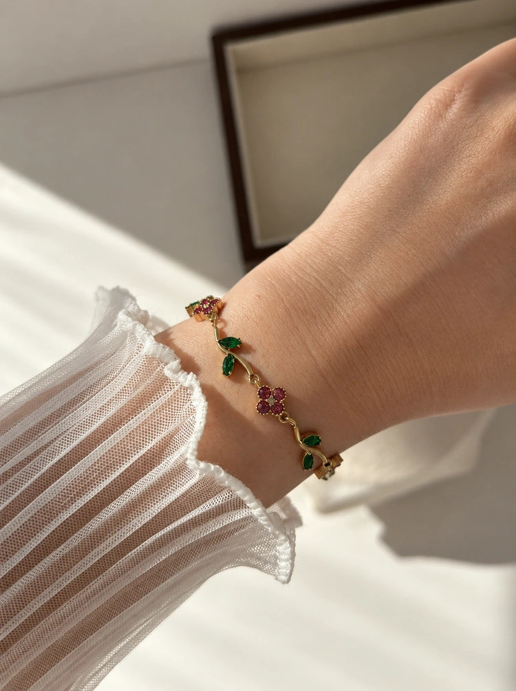 Gardenia Armband aus 14k vergoldetem Edelstahl mit rosa Blüten und grünen Blättern, getragen am Handgelenk mit weißer Tüll-Manschette[cite: 5, 6]