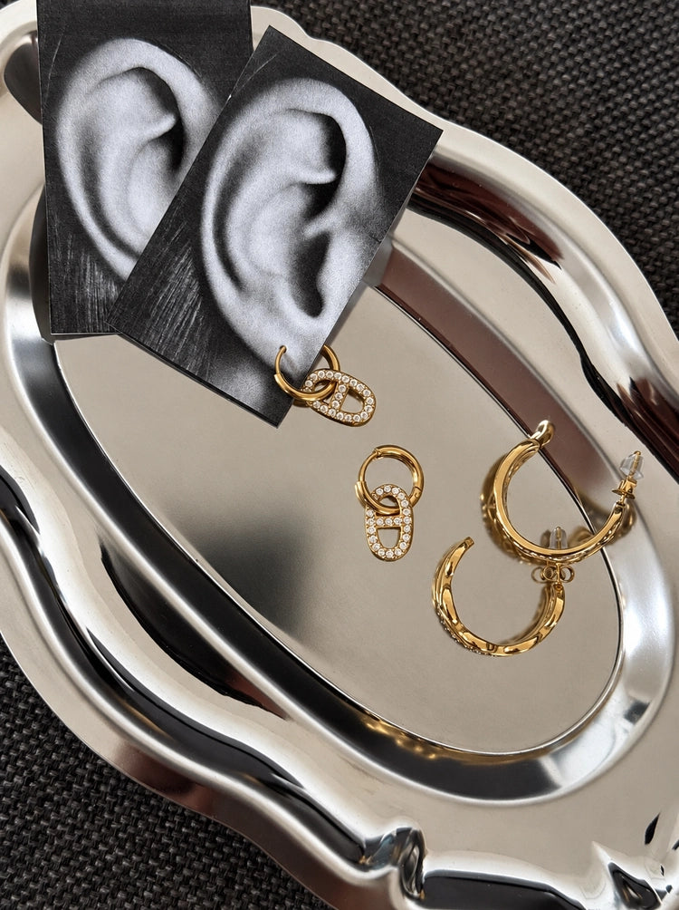 Giulia Creolen Ohrringe in Gold mit weiteren Ohrringen arrangiert auf schwarzem Untergrund.