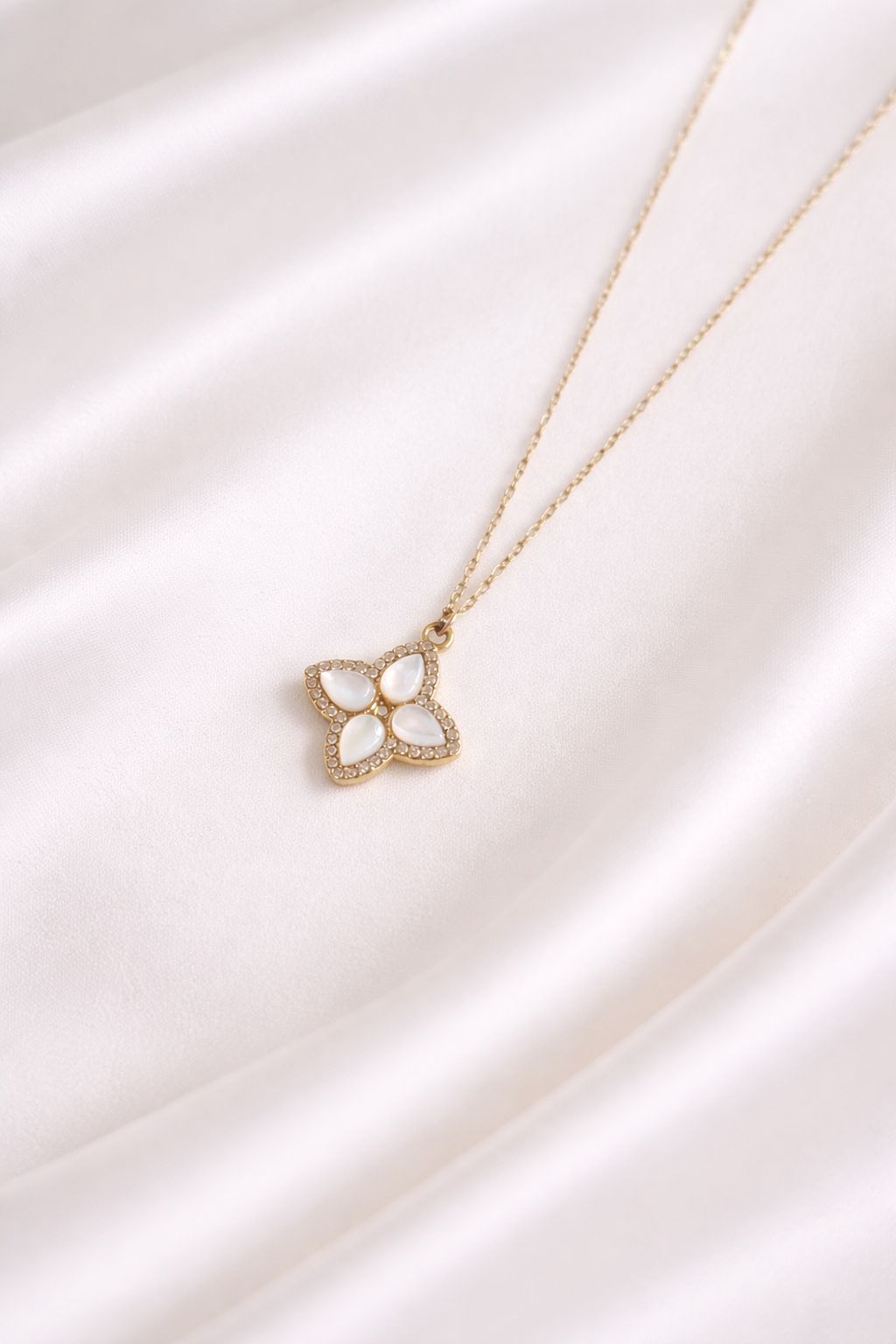 Nahaufnahme der Cleo Halskette auf glänzendem Satin. Elegantes Blumen-Motiv mit weißem Perlmutt und Zirkonia-Halo an einer feinen vergoldeten Edelstahlkette.