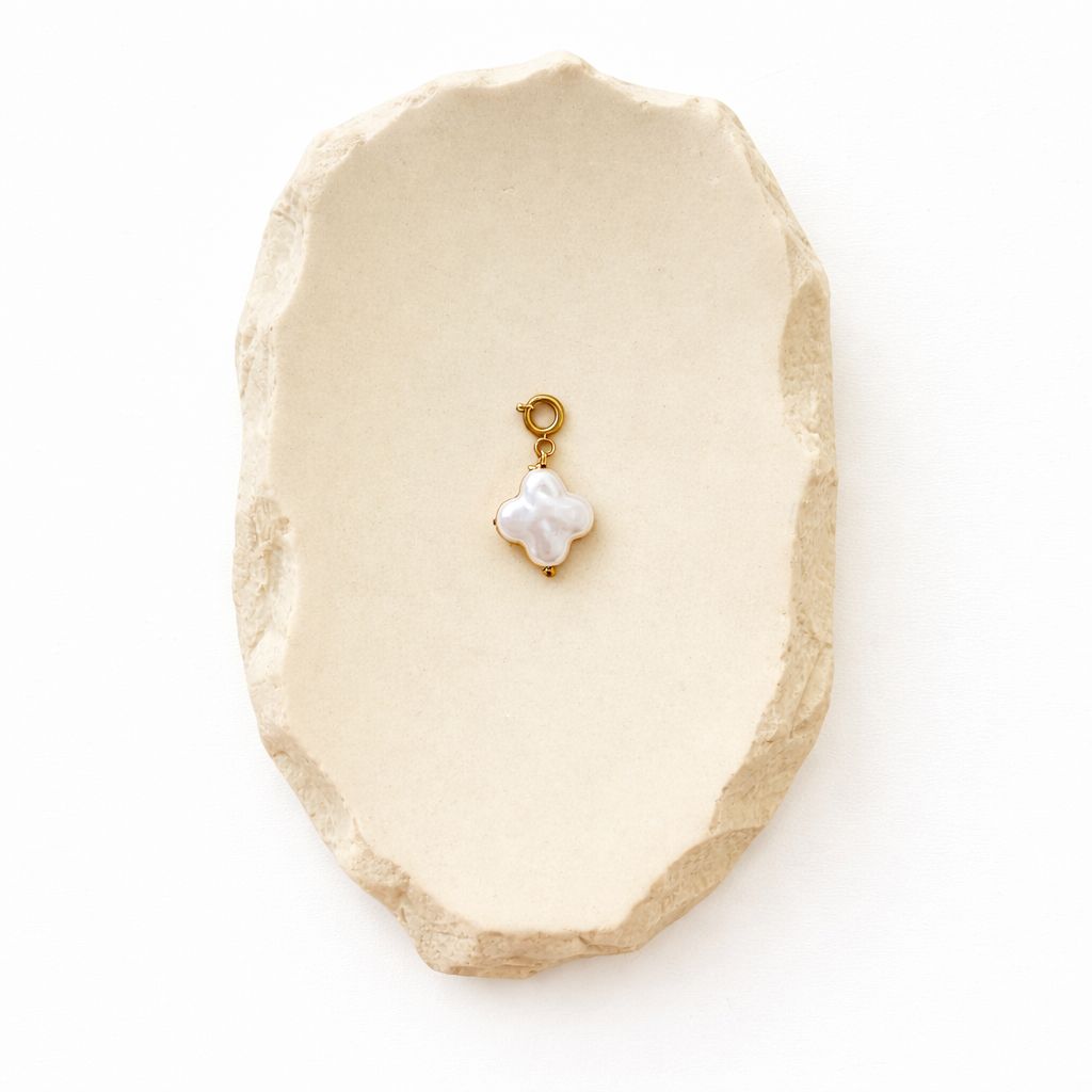 Eleganter Kleeblatt-Anhänger aus weißem Perlmutt und Edelstahl auf einer dekorativen cremefarbenen Steinschale für eine hochwertige Schmuckpräsentation.