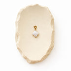 Eleganter Kleeblatt-Anhänger aus weißem Perlmutt und Edelstahl auf einer dekorativen cremefarbenen Steinschale für eine hochwertige Schmuckpräsentation.