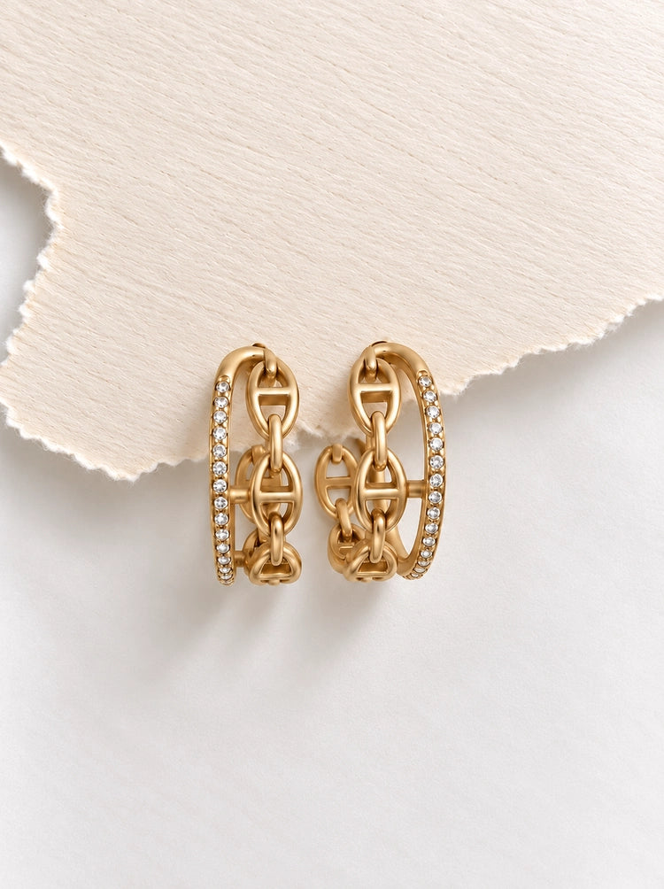 Leona Luxe Ohrringe in Gold auf weißem Seidenstoff mit Zirkonia-Pavé und Ankergliedern.