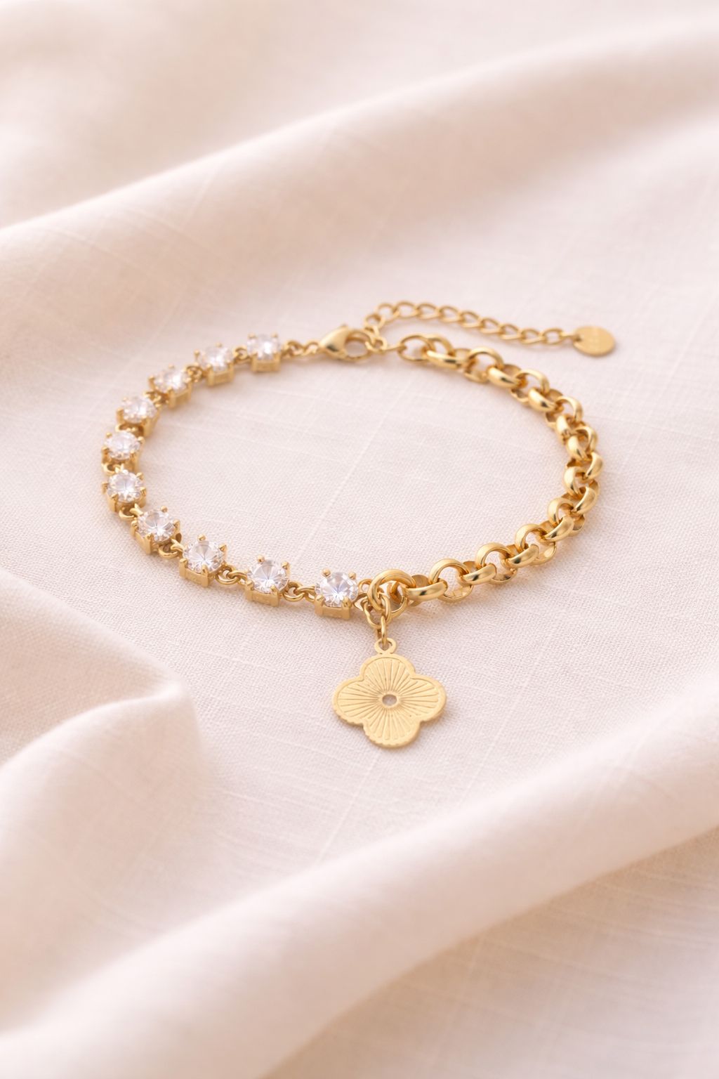Liora Hybrid-Armband flach liegend auf hellem Leinenstoff. Sichtbar sind die funkelnden Zirkonia-Steine, der 14k vergoldete Kleeblatt-Anhänger und der Karabinerverschluss.