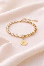 Liora Hybrid-Armband flach liegend auf hellem Leinenstoff. Sichtbar sind die funkelnden Zirkonia-Steine, der 14k vergoldete Kleeblatt-Anhänger und der Karabinerverschluss.