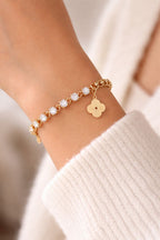 Detailansicht Liora Armband am Handgelenk kombiniert mit weißem Strickpullover. Zeigt das glänzende Tennisarmband-Element und die goldene Gliederkette aus Edelstahl.
