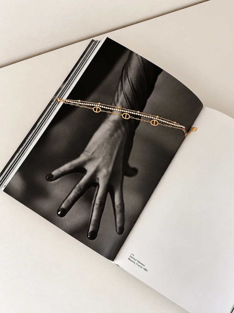 Mehrreihiges Livia Edelstahlarmband in Gold dekoriert auf einem Schwarz-Weiß-Fotobuch.