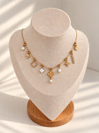 Mirela Charm Halskette in Gold mit Perlen und Charms auf heller Schmuckbüste mit Holzsockel
