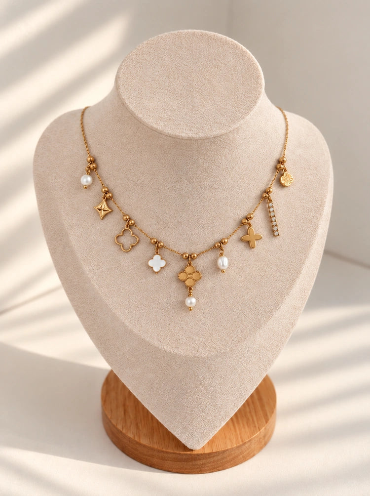 Mirela Charm Halskette in Gold mit Perlen und Charms auf heller Schmuckbüste mit Holzsockel