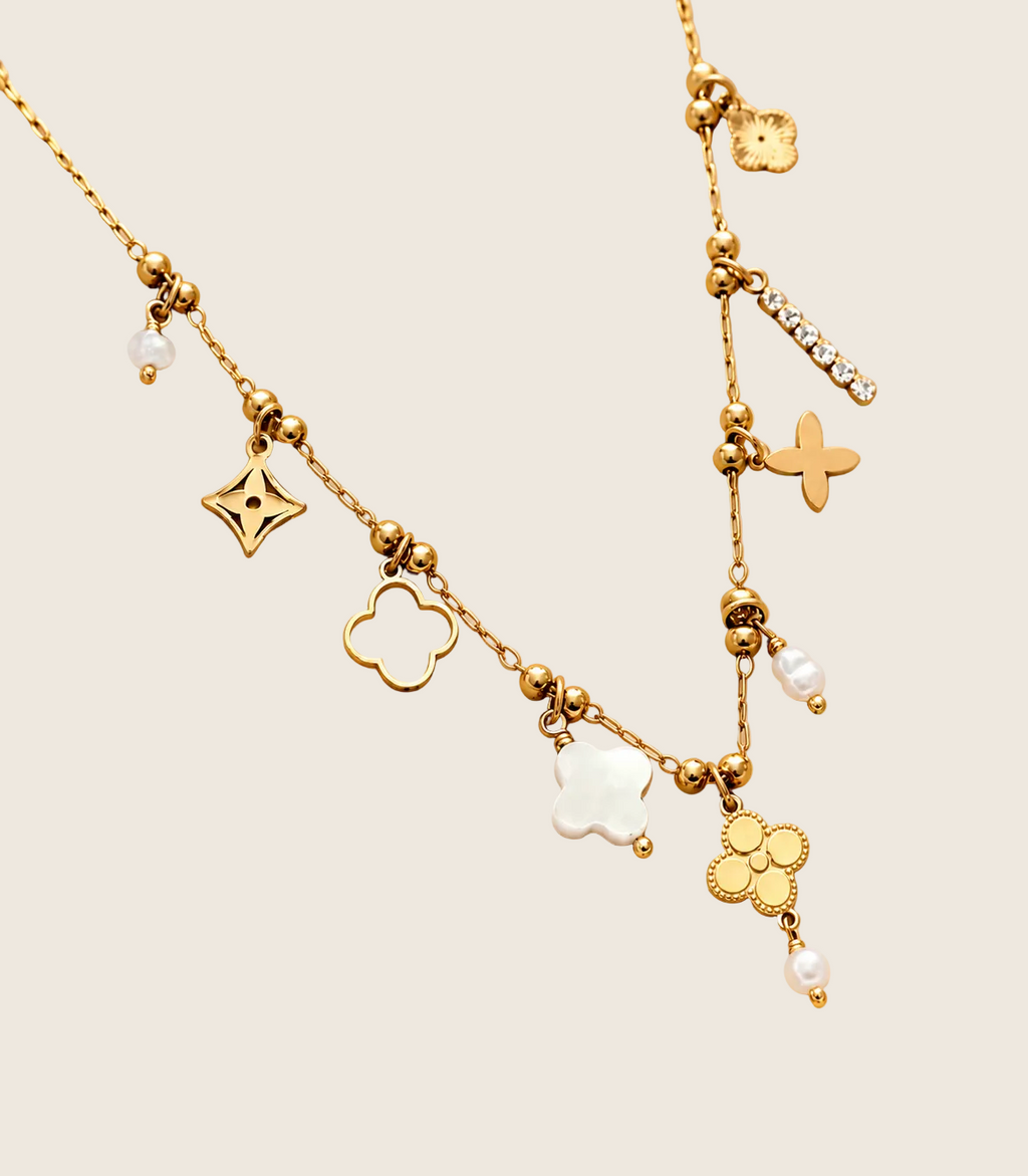 Mirela Charm Halskette in Gold mit Perlmutt-Kleeblatt und Perlen auf cremefarbenem Seidensatin
