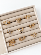 Muse V-Ring aus 14k vergoldetem Edelstahl präsentiert in einm beigen Samt-Schmucktablett neben weiteren Goldringen.