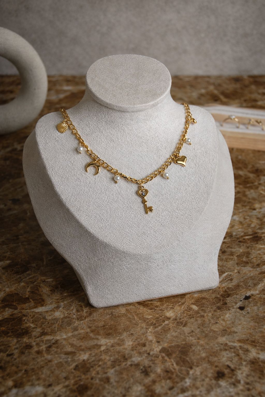 Elegante goldene Gliederkette Mystic Key auf einer Schmuckbüste, verziert mit Anhängern wie Herz-Schlüssel, Mond und Sonne sowie kleinen Perlen-Elementen.