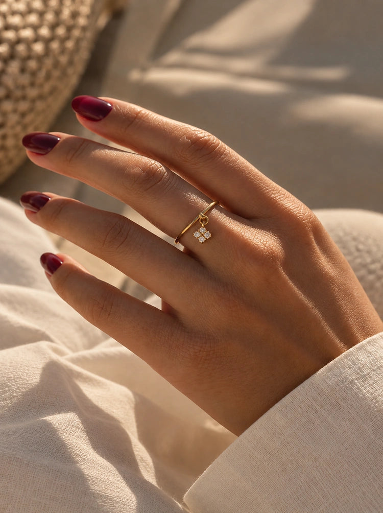 Hand am Strand trägt den Nala Ring in Gold mit Mini-Kleeblatt-Anhänger aus Zirkonia