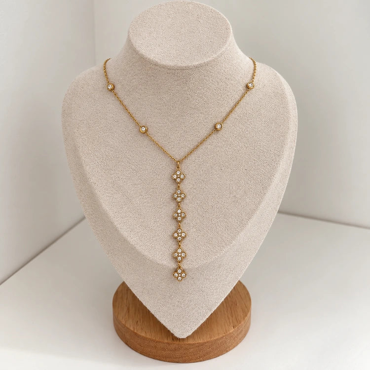 Nymea Y-Halskette in Gold mit Kleeblatt-Anhänger auf heller Schmuckbüste mit Holzsockel