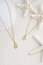 Aurora Halskette mit Perlmutt-Anhänger auf weißem Sand mit Seesternen.