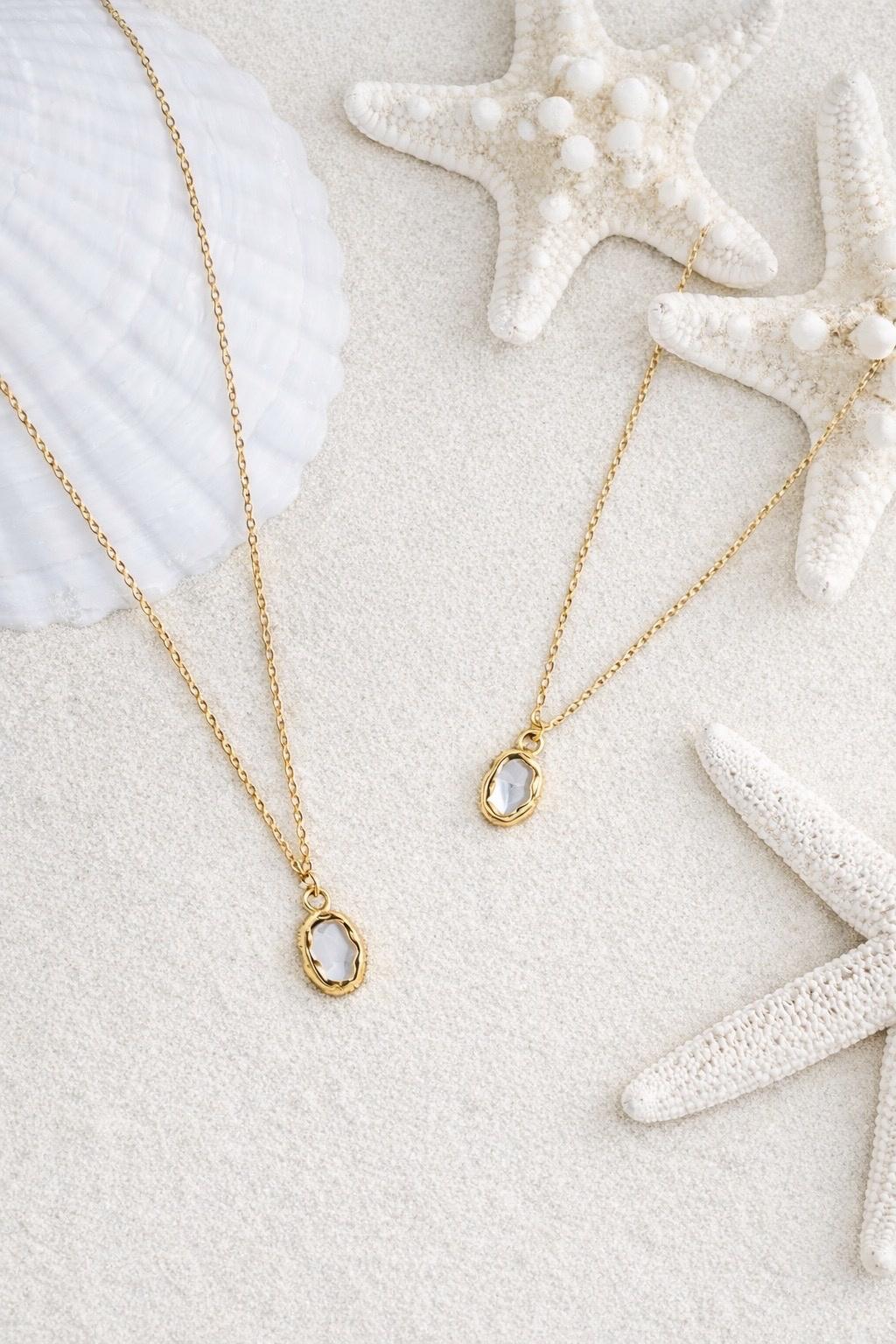 Aurora Halskette mit Perlmutt-Anhänger auf weißem Sand mit Seesternen.