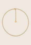 Shine Collier aus Edelstahl mit funkelnden Zirkonia-Steinen in Goldoptik auf beigem Hintergrund.