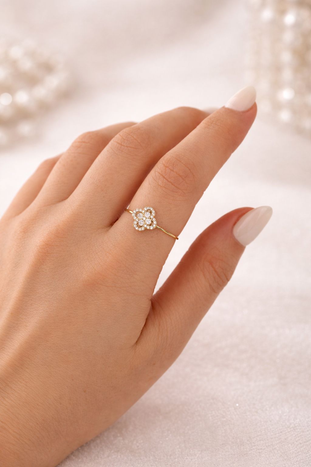 Nahaufnahme der Hand mit dem Vittoria Ring am Zeigefinger. Der schmale, goldene Ring mit glitzerndem Glücksklee-Motiv unterstreicht ein elegantes Nageldesign und passt perfekt zum modernen Schmuck-Stacking.